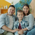 Portrait of happy young family mother, father and son sitting on sofa at home smiling looking at camera. People, lifestyle and togetherness concept.